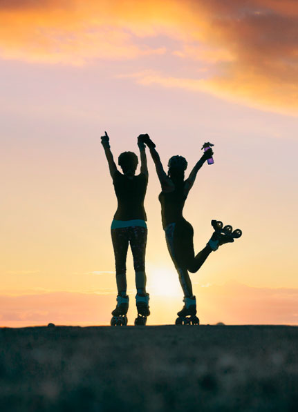 Silhouette of two women on Powerslide inline skates and protective gear looking at the horizon 