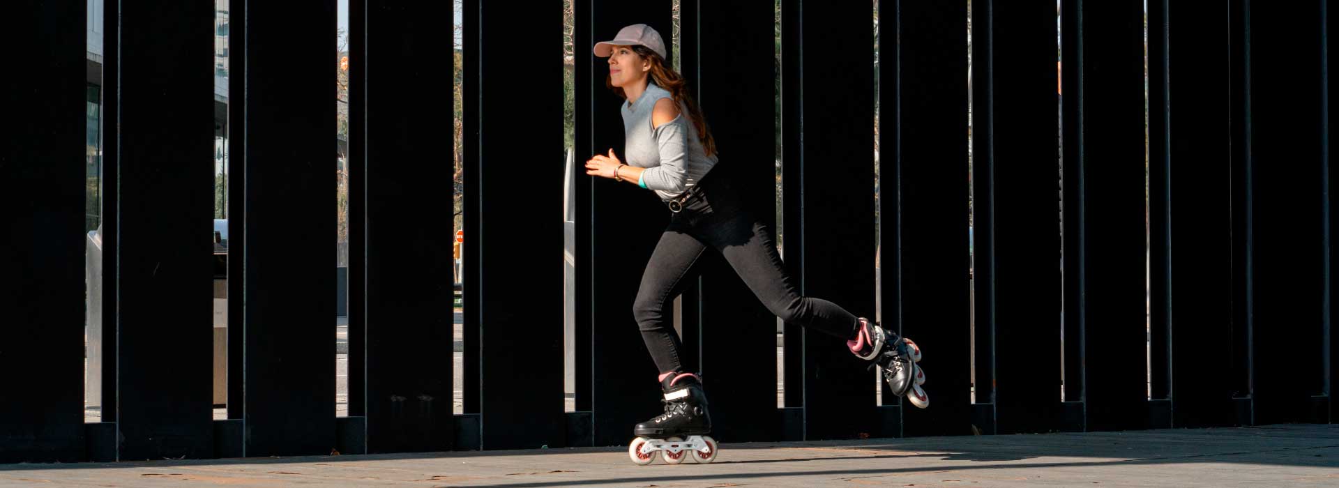 Woman in a pink hat grey shirt and black pants skating on 3-wheel Powerslide inline skates