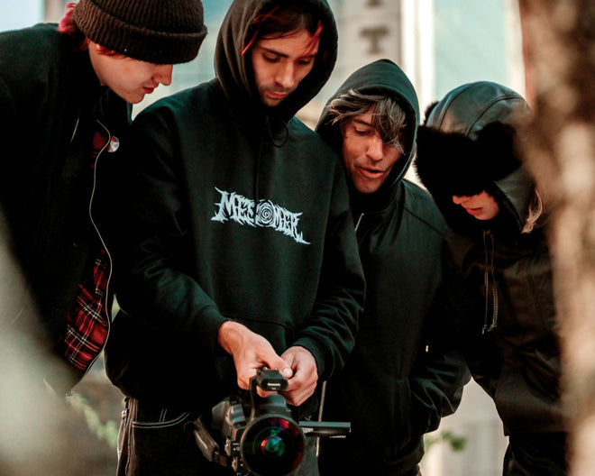 Four individuals in hoodies looking at a device with a building in the background