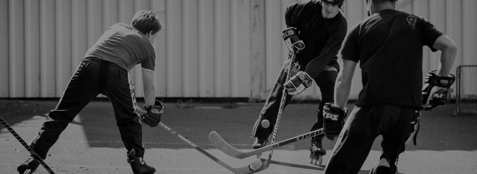 Three men playing street hockey holding sticks and wearing Powerslide inline hockey skates