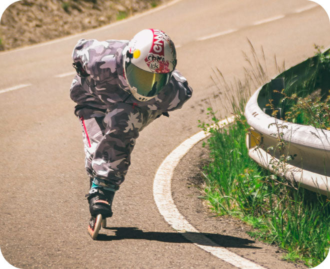 A person with a helmet and face shield rolls down a hill at high speeds on inline skates 