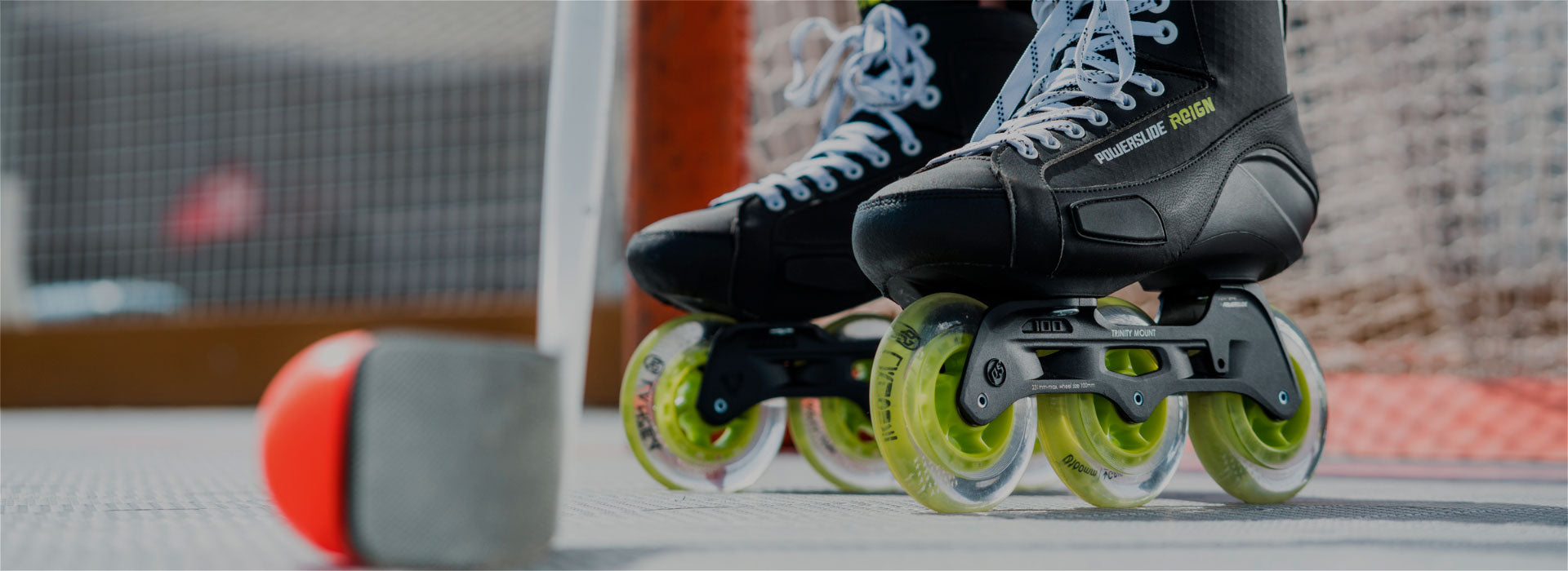 A close-up image of 3-wheel Powerslide Reign inline roller hockey skates with a hockey net in the background