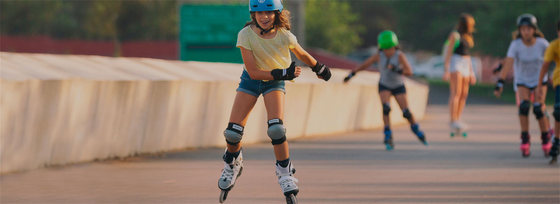 Young girl with a smile on her face rolls on Powerslide inline kids skates with other children skating in the background