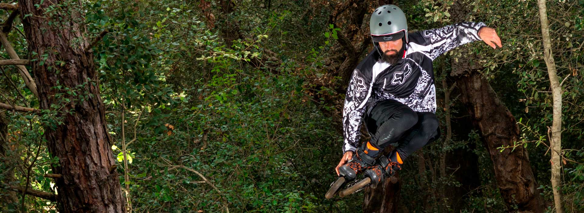 A person with a helmet gets big air on Powerslide SUV inline skates with a forest in the background