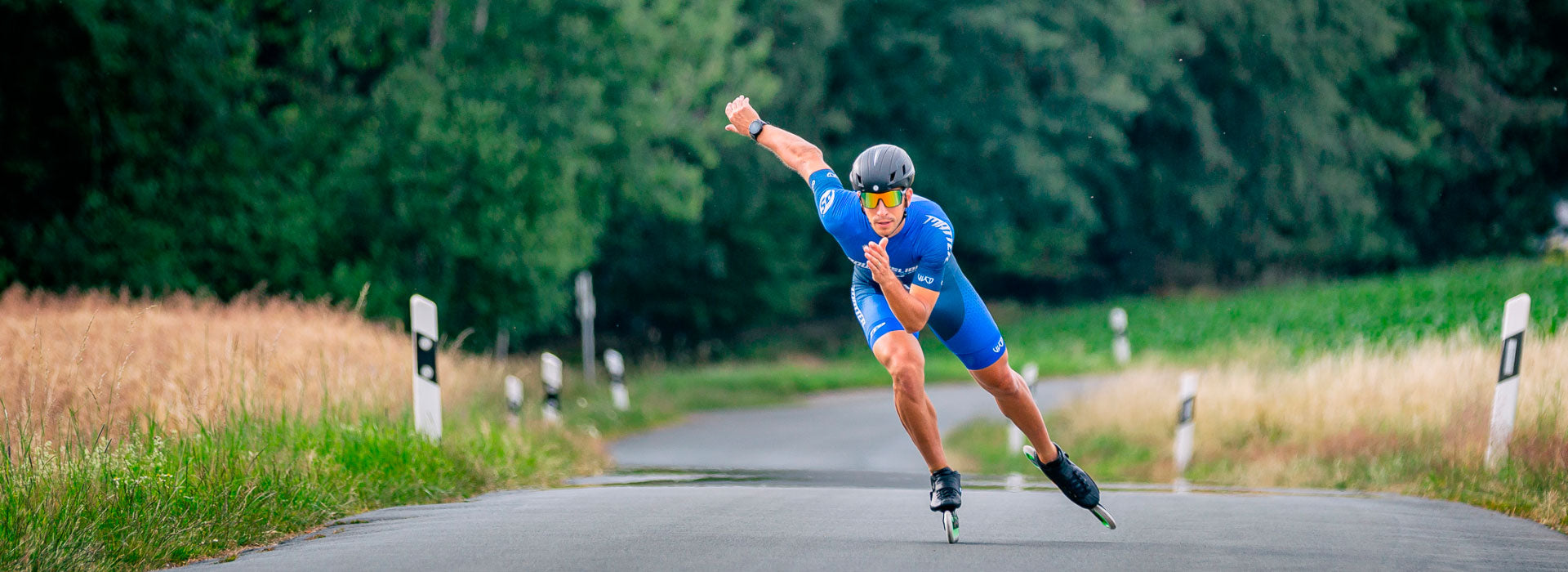 An inline speed skater with a black helmet and sunglasses wearing Powerslide inline race skates mid-stride skating down a road