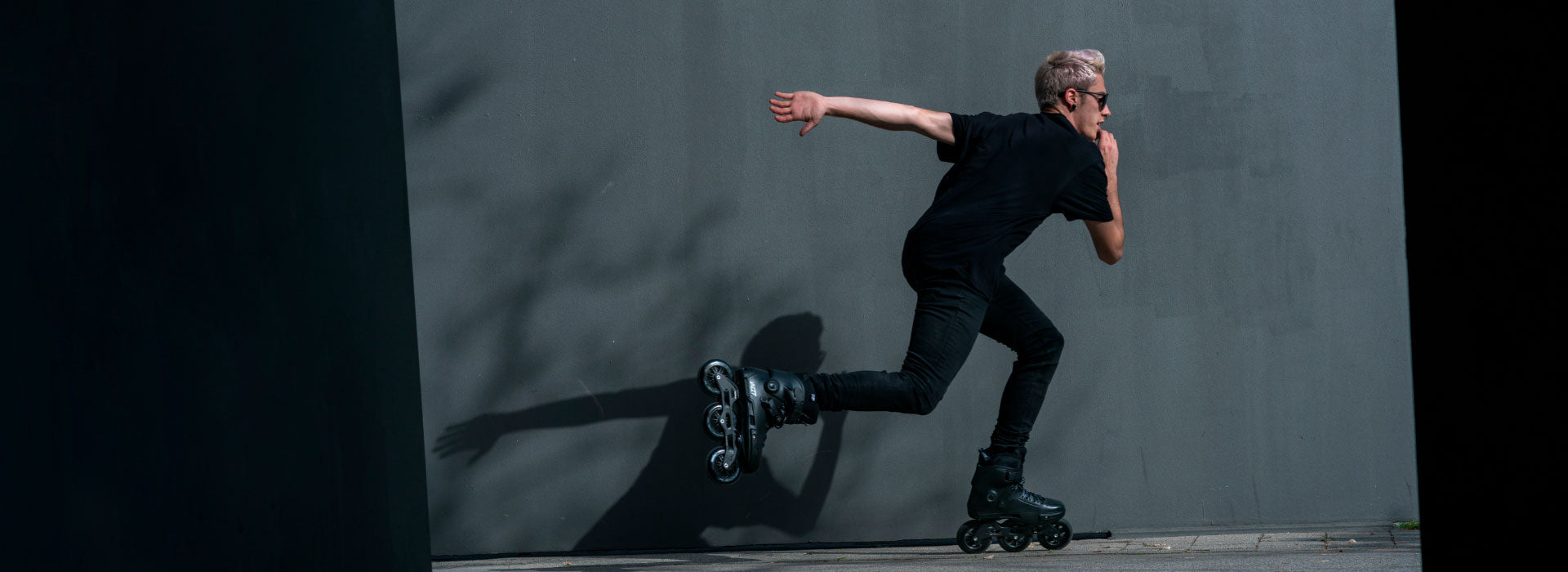 Man with sunglasses a black shirt and black pants skating on black Powerslide inline skates
